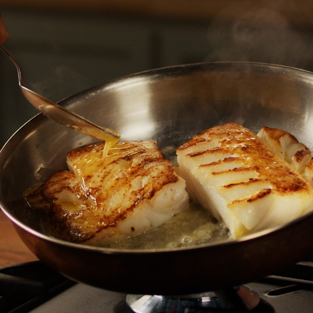 Een gebakken visfilet in een pan met gesmolten boter